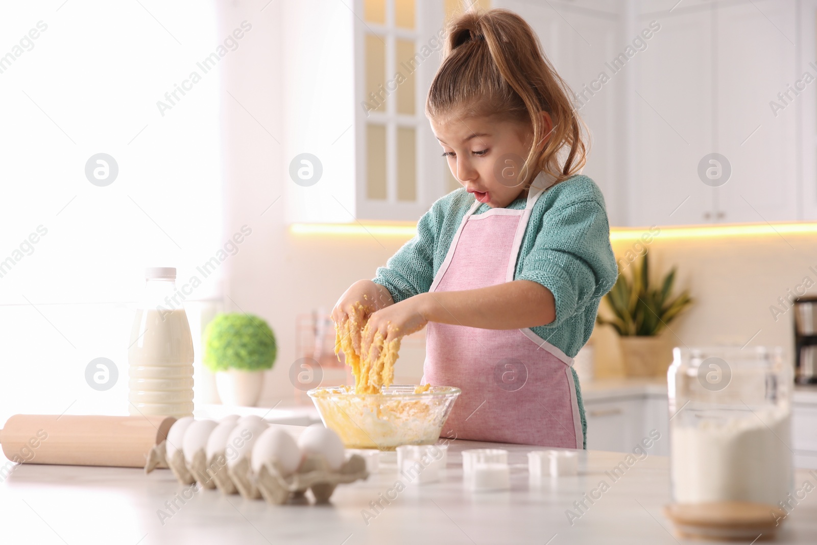 Photo of Little girl making dough at table in kitchen