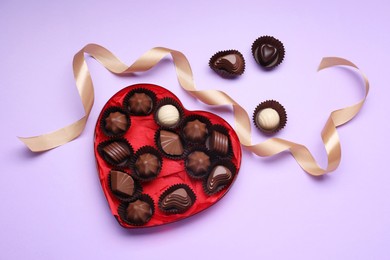 Photo of Heart shaped box with delicious chocolate candies and ribbon on lilac background, flat lay