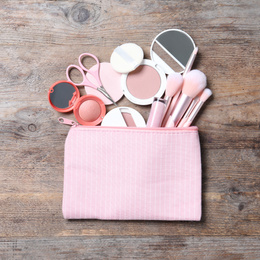 Photo of Cosmetic bag with makeup products and beauty accessories on wooden background, flat lay