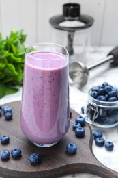Photo of Glass of blueberry smoothie and fresh berries on white marble table