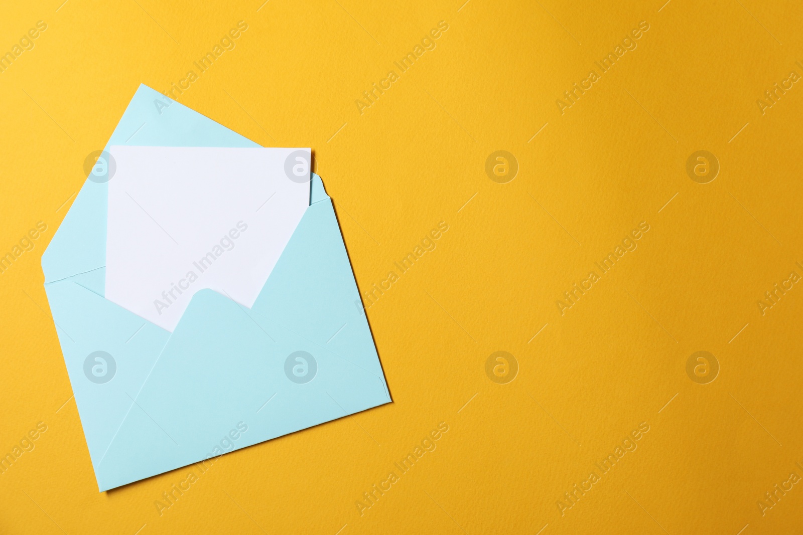Photo of Blank sheet of paper in open letter envelope on orange background, top view. Space for text