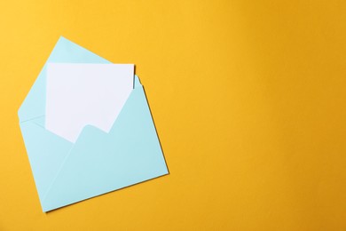 Blank sheet of paper in open letter envelope on orange background, top view. Space for text