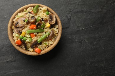 Photo of Delicious bulgur with vegetables and mushrooms in bowl on black table, top view. Space for text