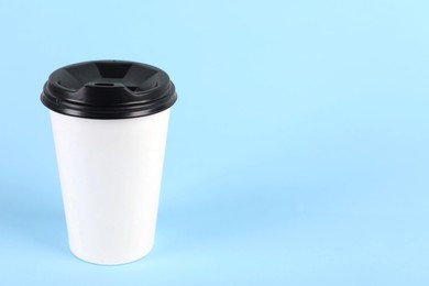 Photo of Paper cup with plastic lid on light blue background, space for text. Coffee to go