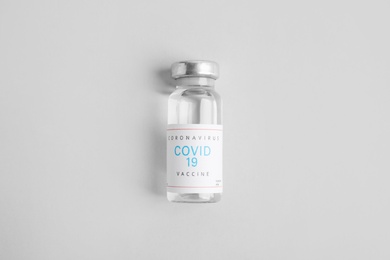 Vial with coronavirus vaccine on light background, top view