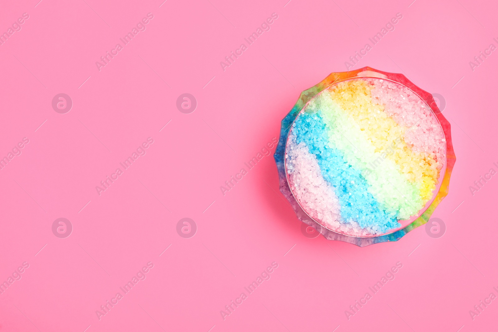 Photo of Rainbow shaving ice in glass dessert bowl on pink background, top view. Space for text