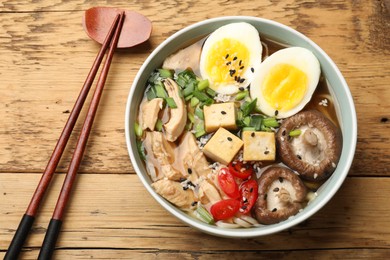 Photo of Bowl of delicious ramen and chopsticks on wooden table, flat lay. Noodle soup