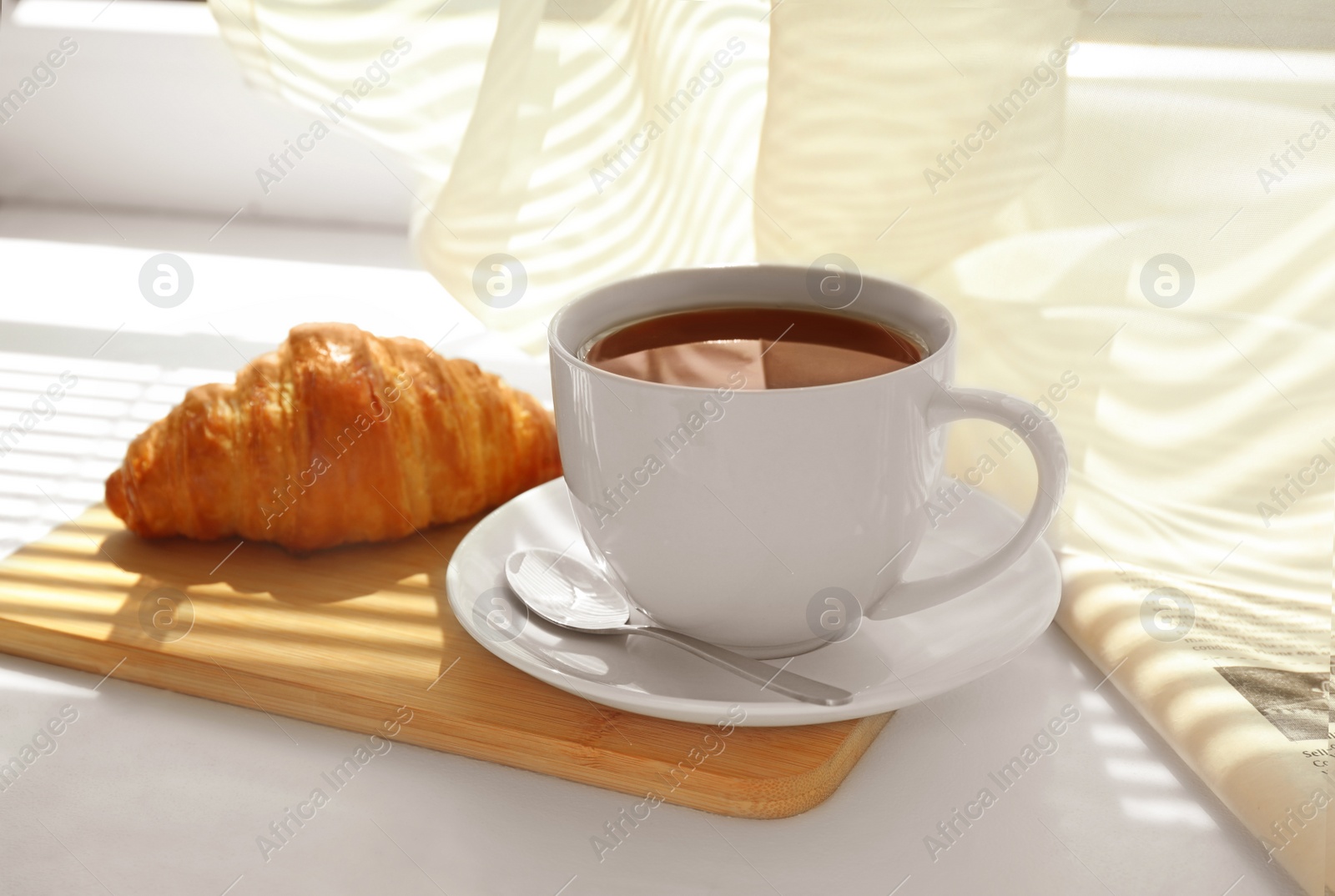 Photo of Delicious breakfast with croissant and cup of coffee on window sill