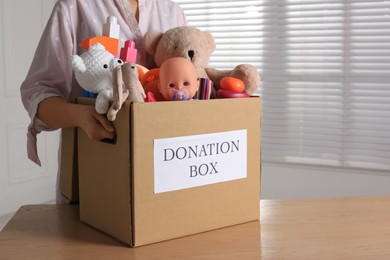 Woman holding donation box with child goods indoors, closeup. Space for text
