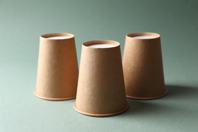 Three paper cups on pale olive background. Thimblerig game