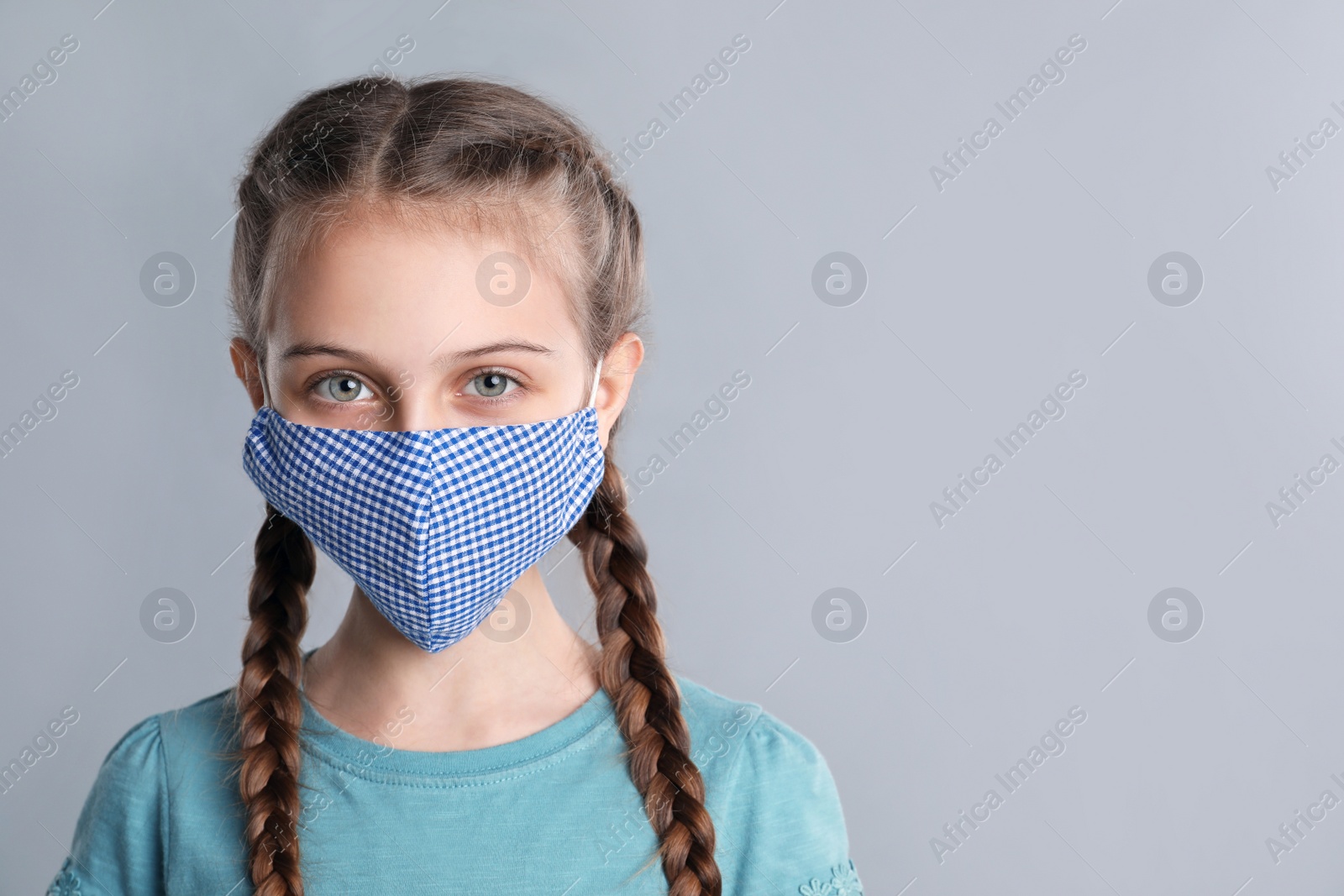 Photo of Girl wearing protective mask on grey background, space for text. Child's safety from virus