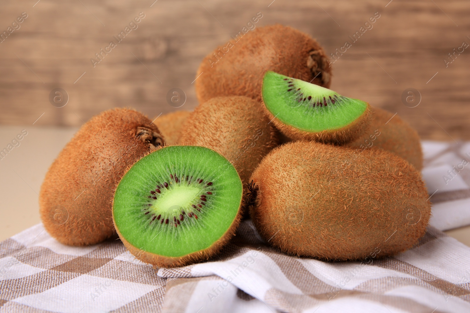 Photo of Heap of whole and cut fresh kiwis on checkered tablecloth, closeup