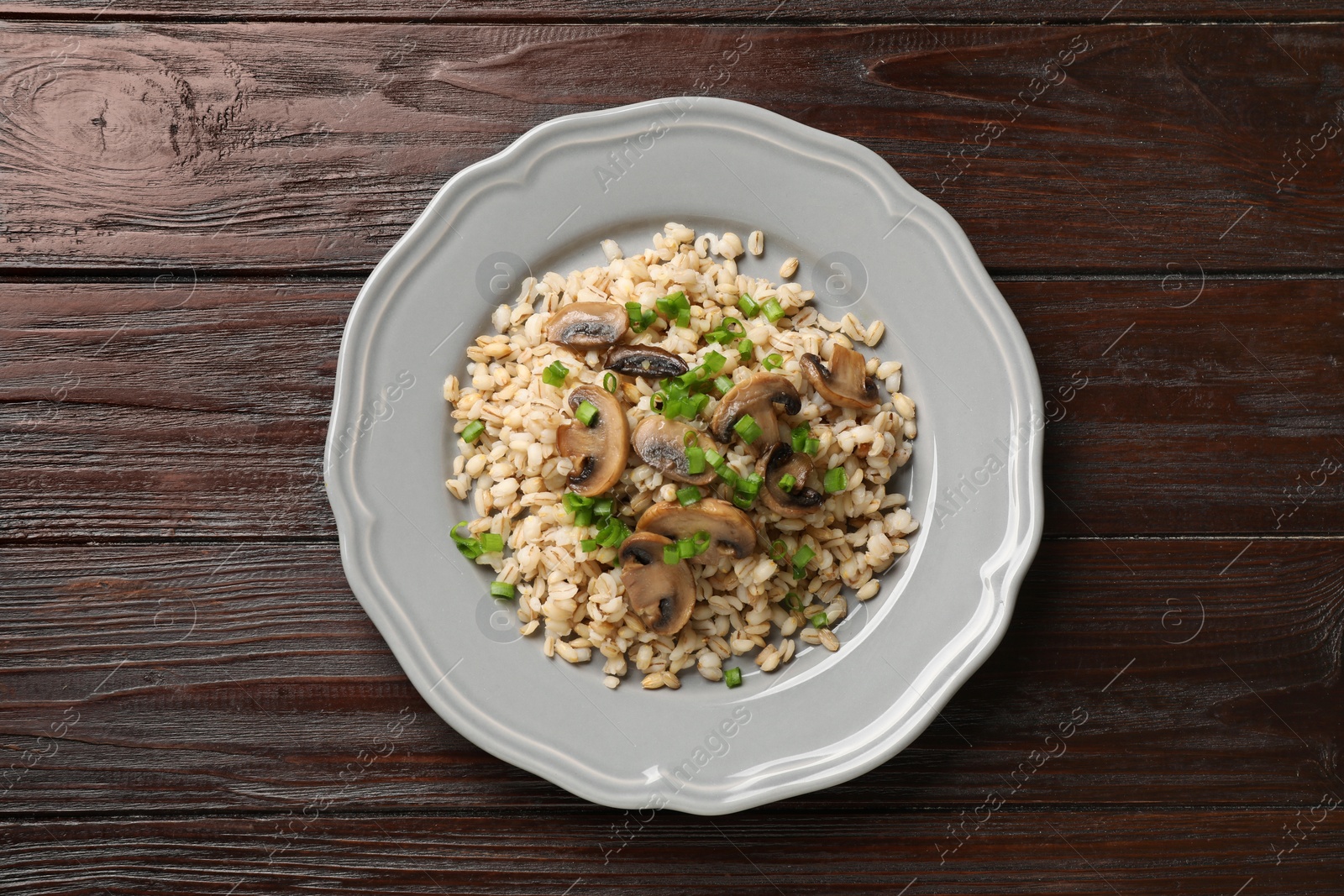 Photo of Delicious pearl barley with onion and mushrooms on wooden table, top view