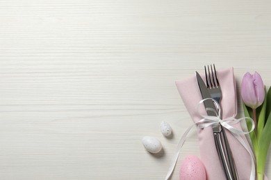 Photo of Cutlery set, painted eggs and beautiful flower on white wooden table, flat lay with space for text. Easter celebration