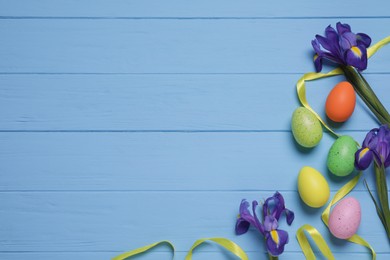 Photo of Flat lay composition with festively decorated Easter eggs and iris flowers on light blue wooden table. Space for text