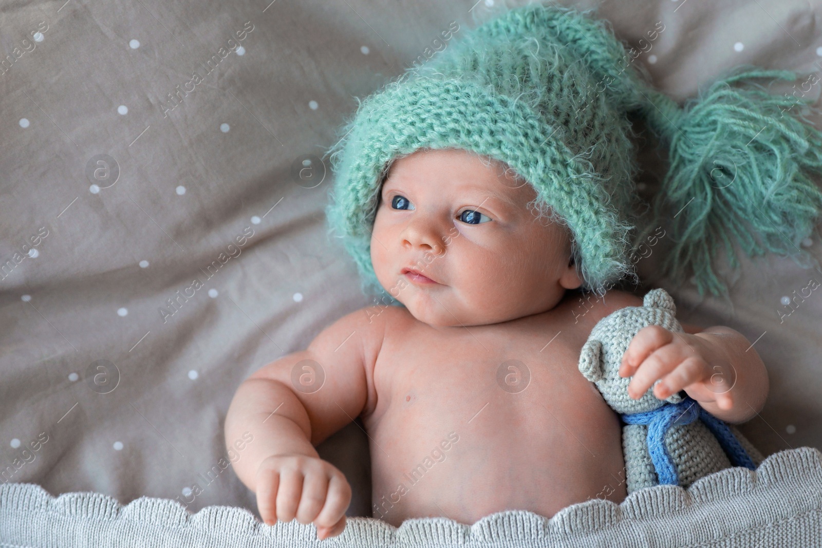 Photo of Cute newborn baby in warm hat with toy lying on bed, top view