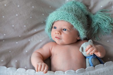 Cute newborn baby in warm hat with toy lying on bed, top view