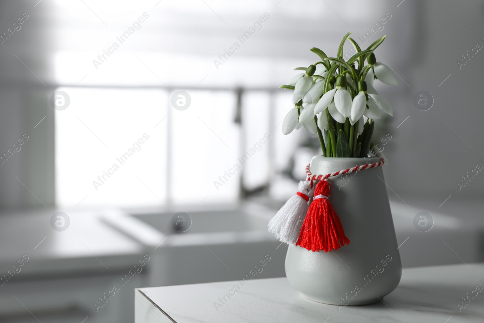 Photo of Beautiful snowdrops with traditional martisor on table indoors, space for text. Symbol of first spring day