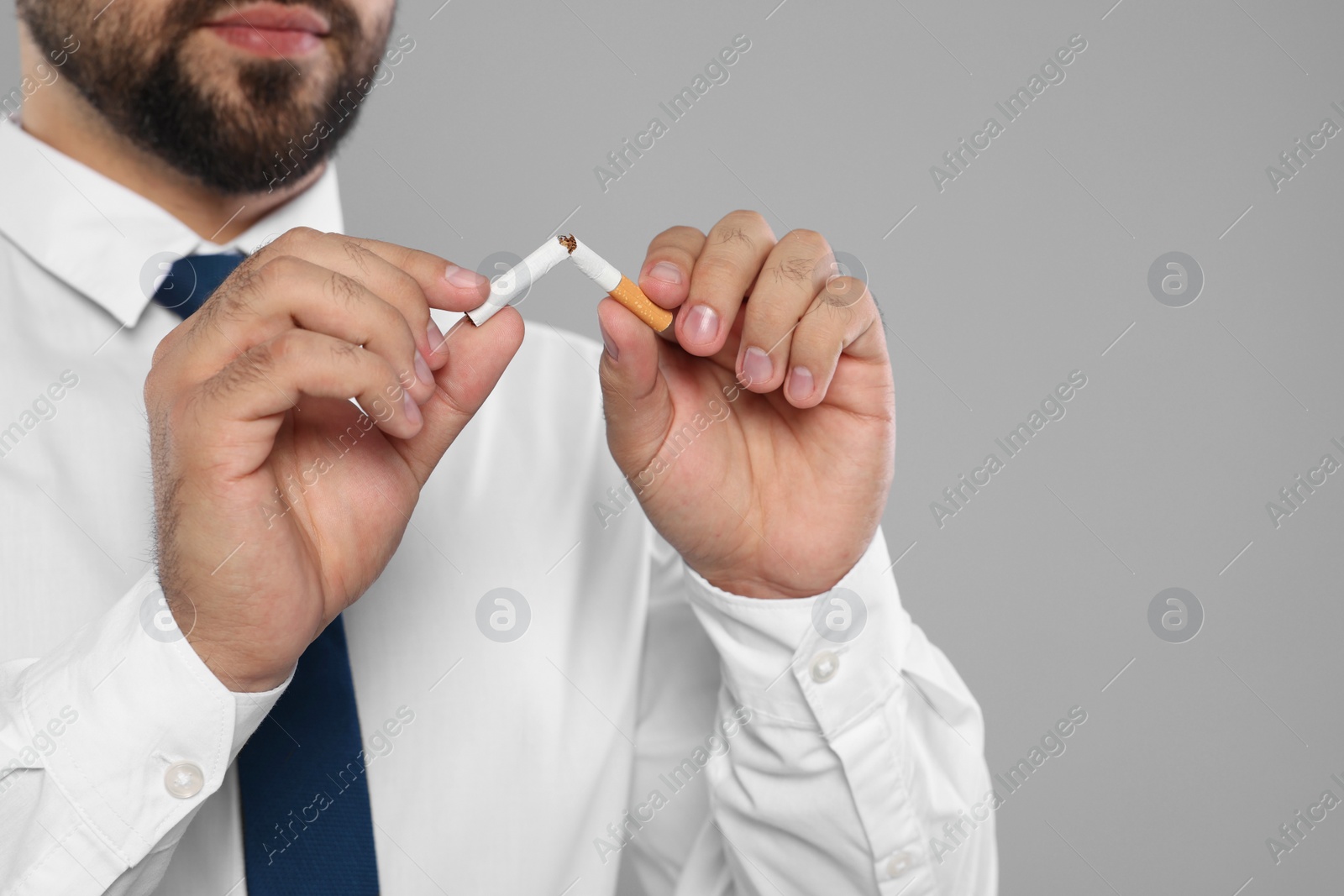 Photo of Stop smoking concept. Man breaking cigarette on light grey background, closeup. Space for text