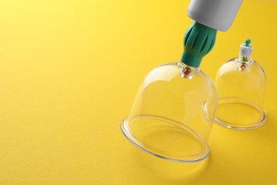 Photo of Plastic cups and hand pump on yellow background, closeup with space for text. Cupping therapy