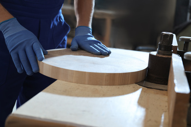 Photo of Professional carpenter grinding piece of wood in workshop, closeup