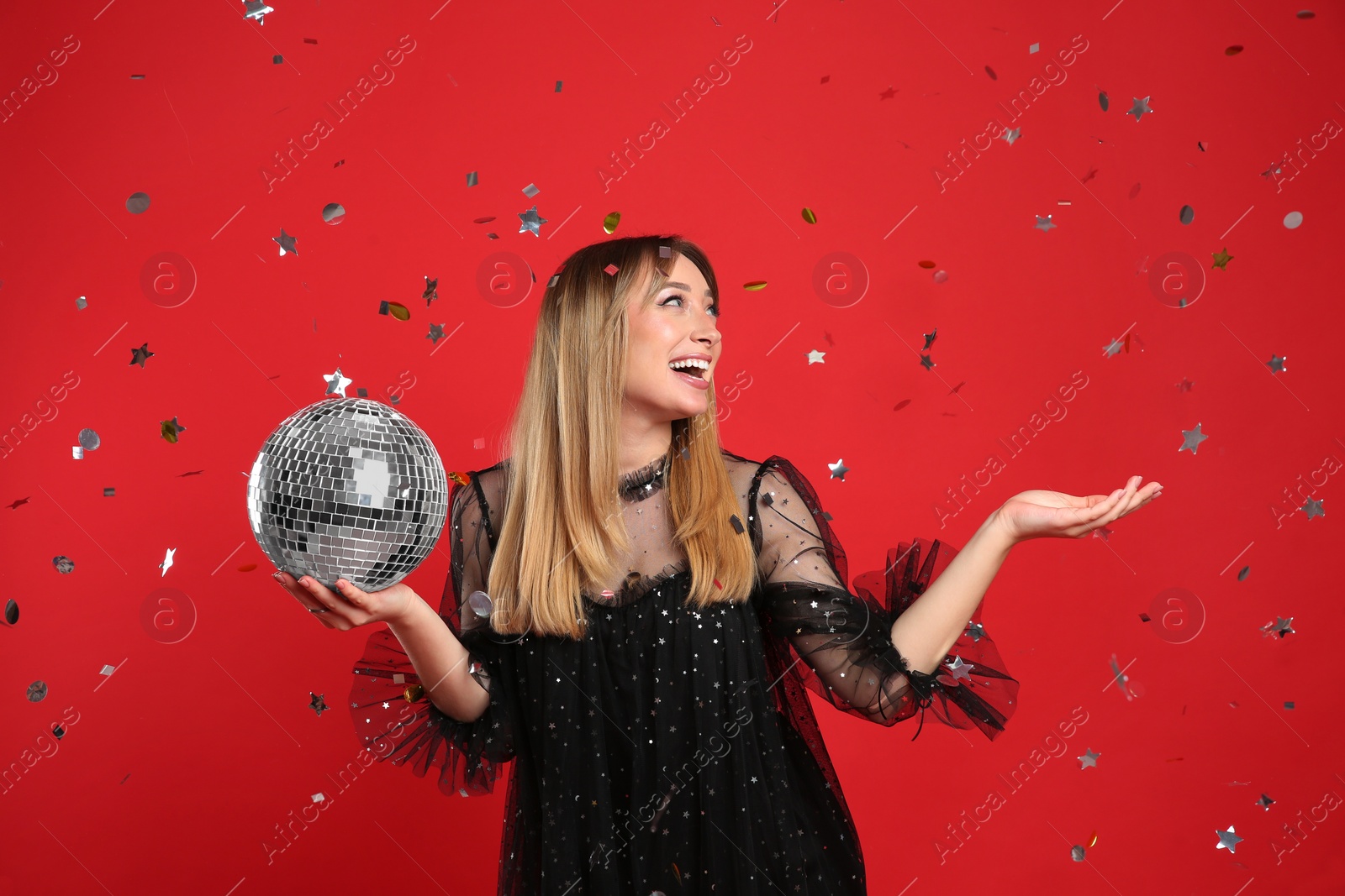 Photo of Happy young woman with disco ball and confetti on red background