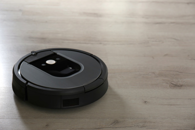 Modern robotic vacuum cleaner on wooden floor. Space for text