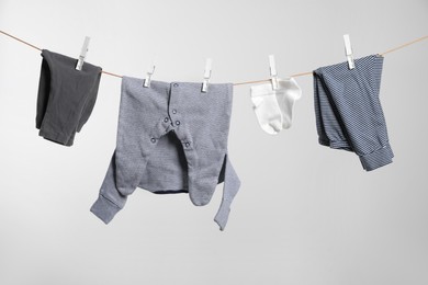 Cute baby clothes drying on washing line against white background