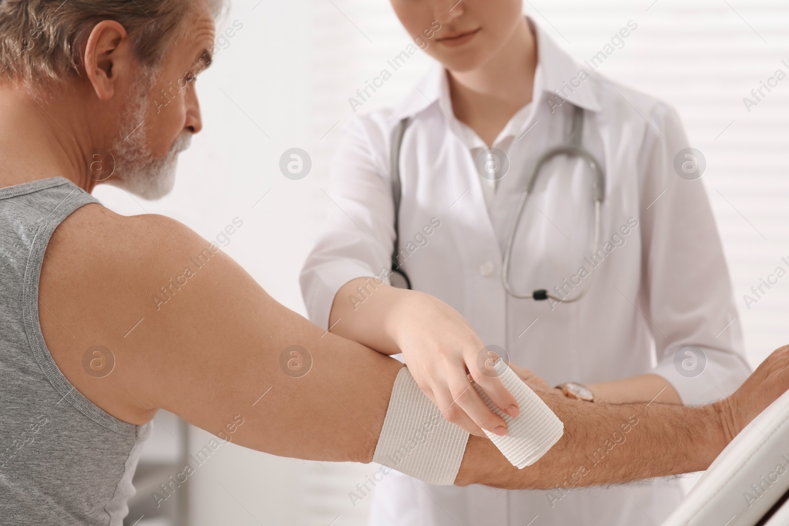 Photo of Orthopedist applying bandage onto patient's elbow in clinic, closeup