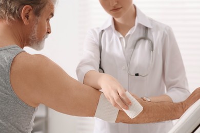 Orthopedist applying bandage onto patient's elbow in clinic, closeup