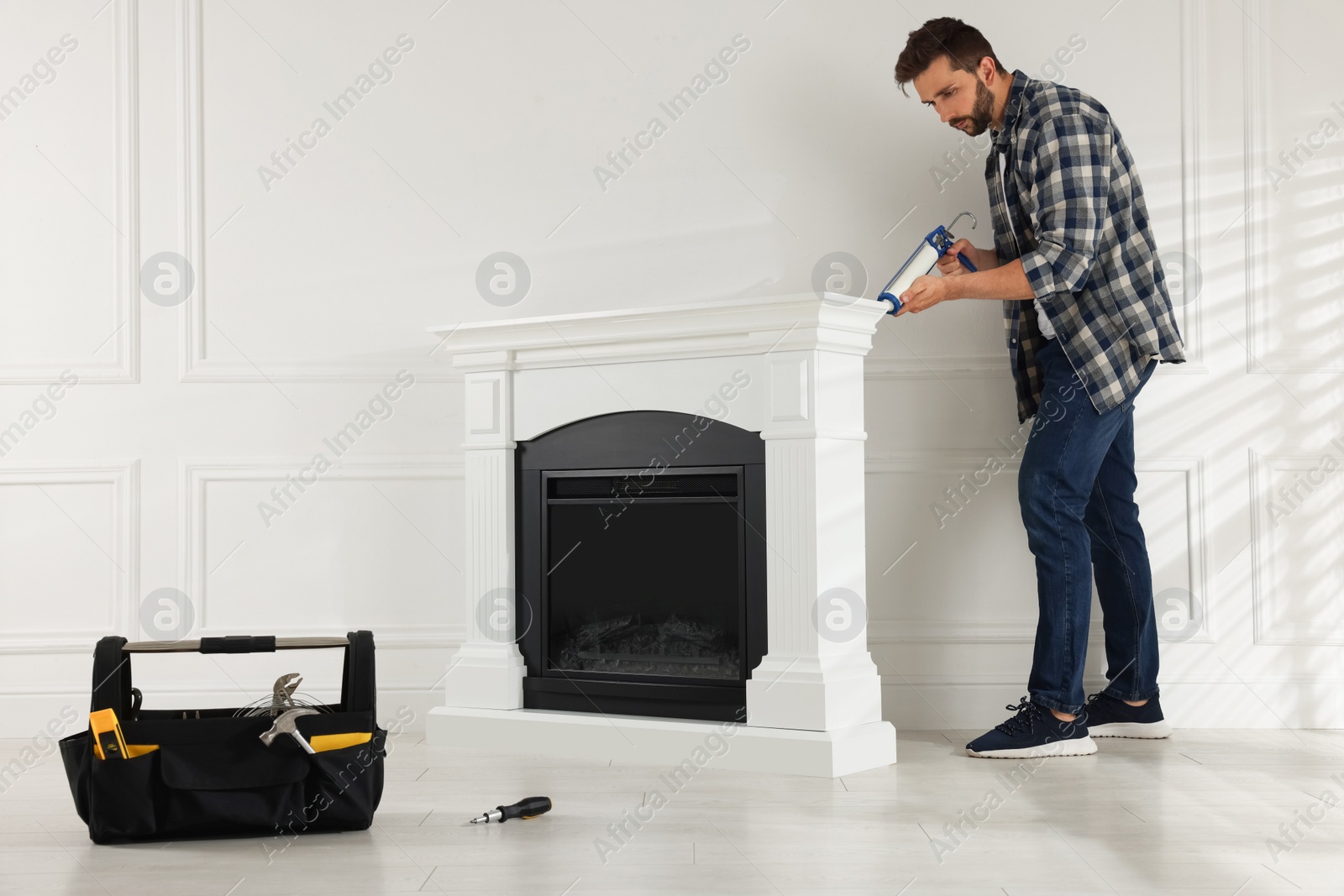 Photo of Man sealing electric fireplace with caulk near white wall in room