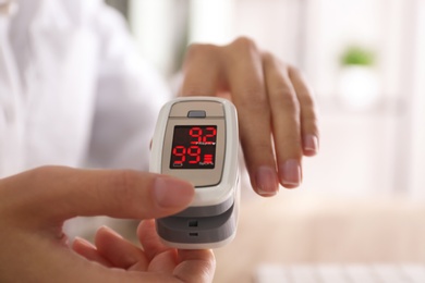 Photo of Woman measuring oxygen level with modern fingertip pulse oximeter at workplace, closeup