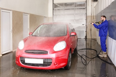 Worker cleaning automobile with high pressure water jet at car wash