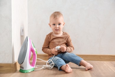 Photo of Little child playing with iron plug near electrical socket at home. Dangerous situation
