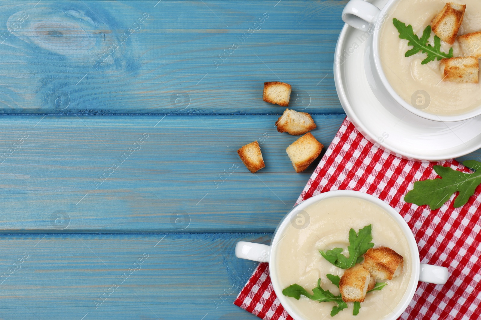 Photo of Bowls with tasty creamy soup of parsnip on light blue wooden table, flat lay. Space for text