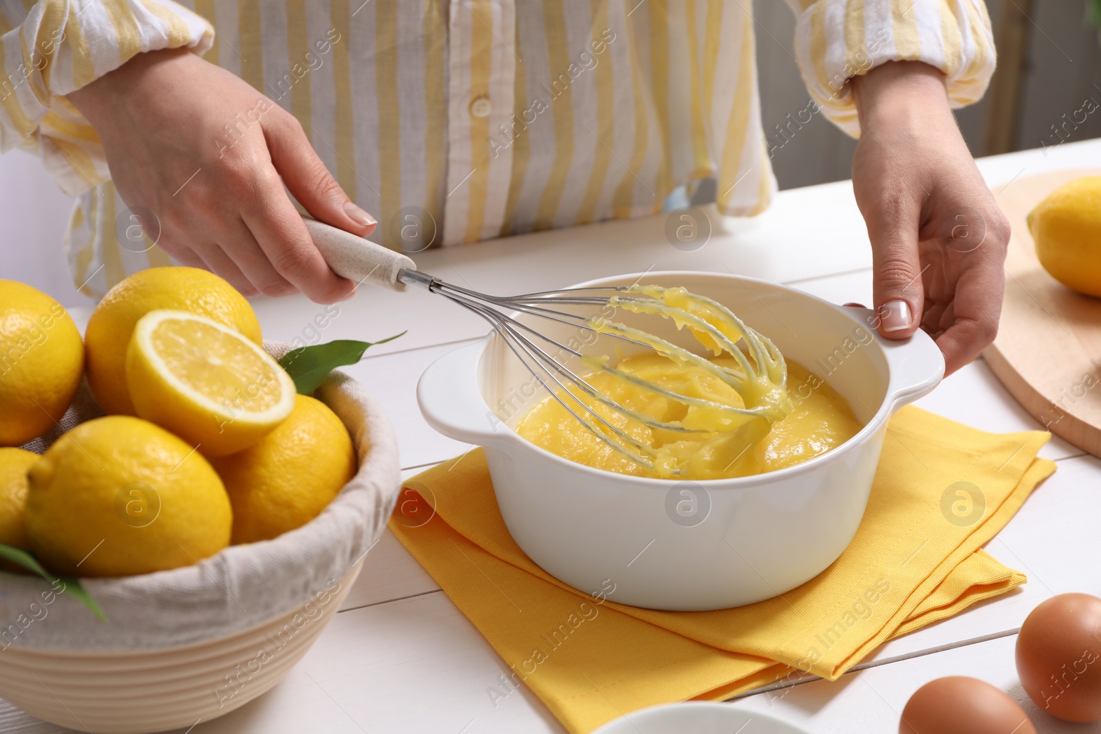 Photo of Woman cooking lemon curd at white wooden table, closeup