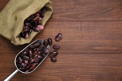 Photo of Metal scoop and sack with dry kidney beans on wooden table, flat lay. Space for text