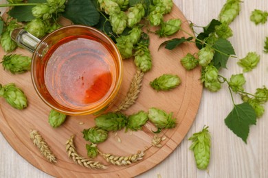 Photo of Mug with beer, fresh hops and ears of wheat on light wooden table, flat lay