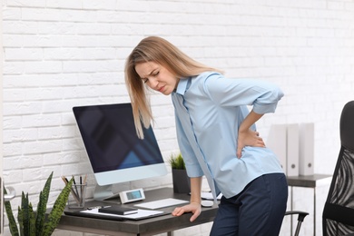 Photo of Young woman suffering from back pain in office