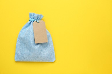 Photo of Light blue burlap bag with tag on yellow background, top view. Space for text