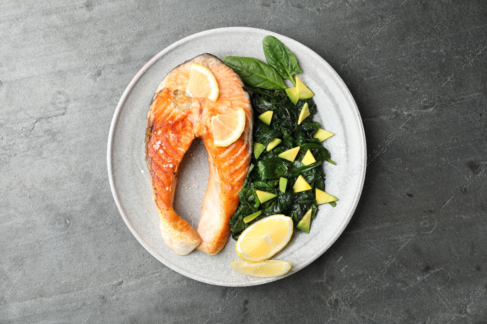 Photo of Tasty salmon with baby spinach on grey table, top view