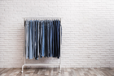 Photo of Rack with stylish jeans near brick wall. Space for text