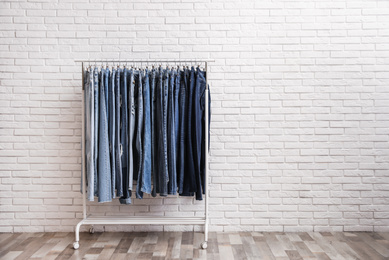 Rack with stylish jeans near brick wall. Space for text