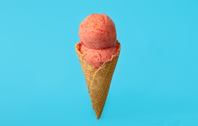 Delicious pink ice cream in waffle cone on light blue background