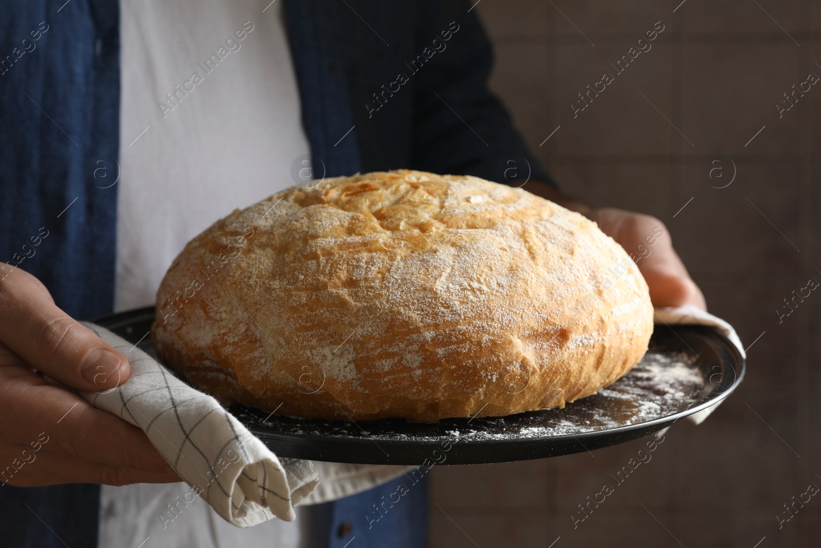 Photo of Man holding loaf of fresh bread on dark background, closeup