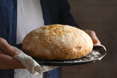 Photo of Man holding loaf of fresh bread on dark background, closeup