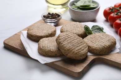 Photo of Raw vegan cutlets and different products on white table