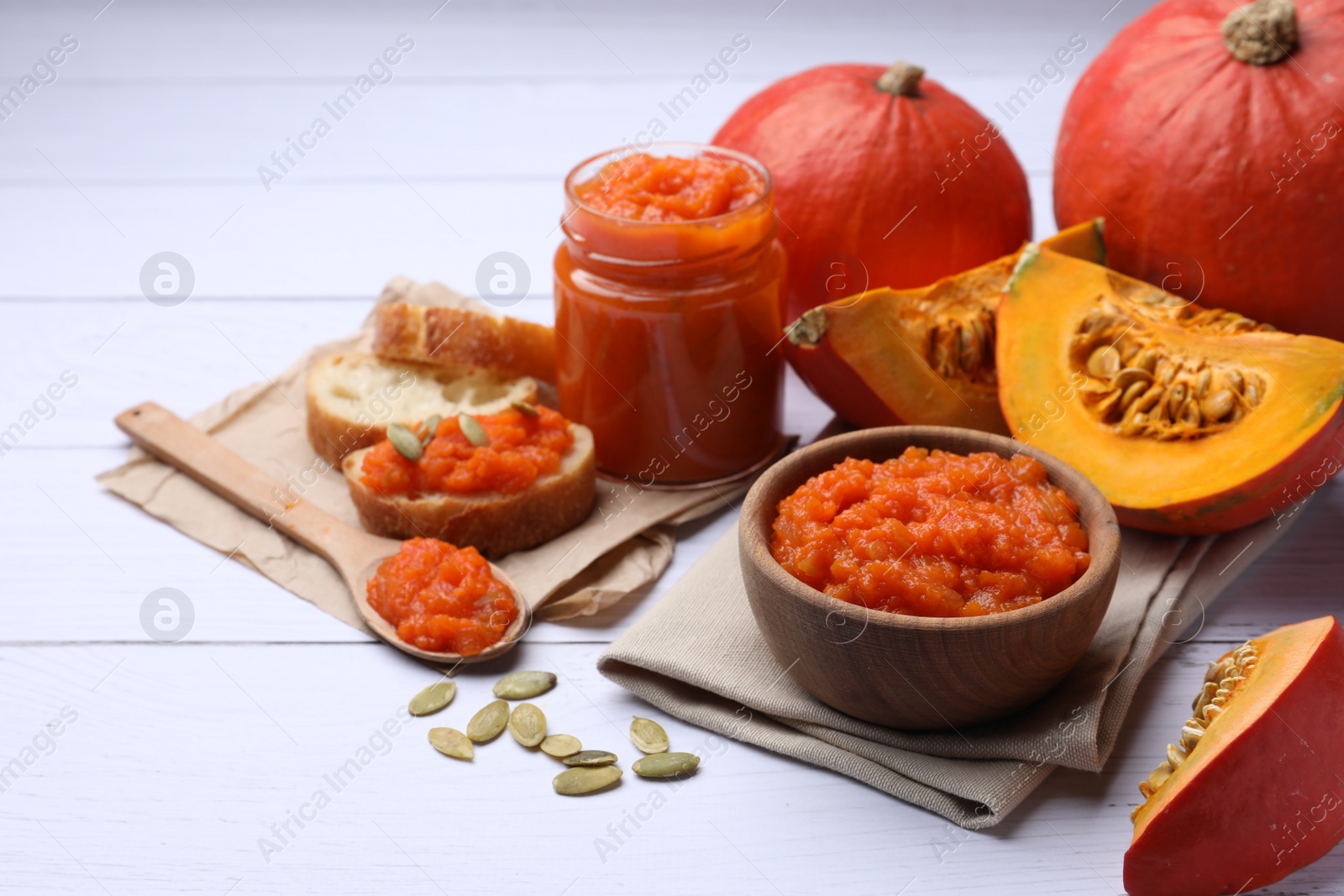 Photo of Delicious pumpkin jam and fresh pumpkins on white wooden table