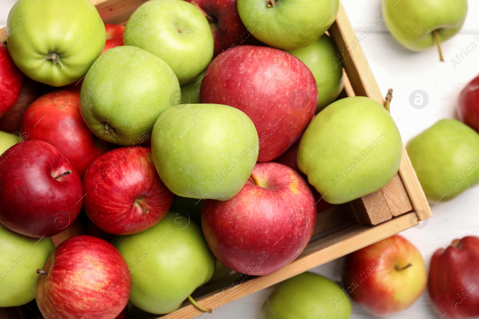 Photo of Wooden crate with ripe red and green apples on white table, flat lay