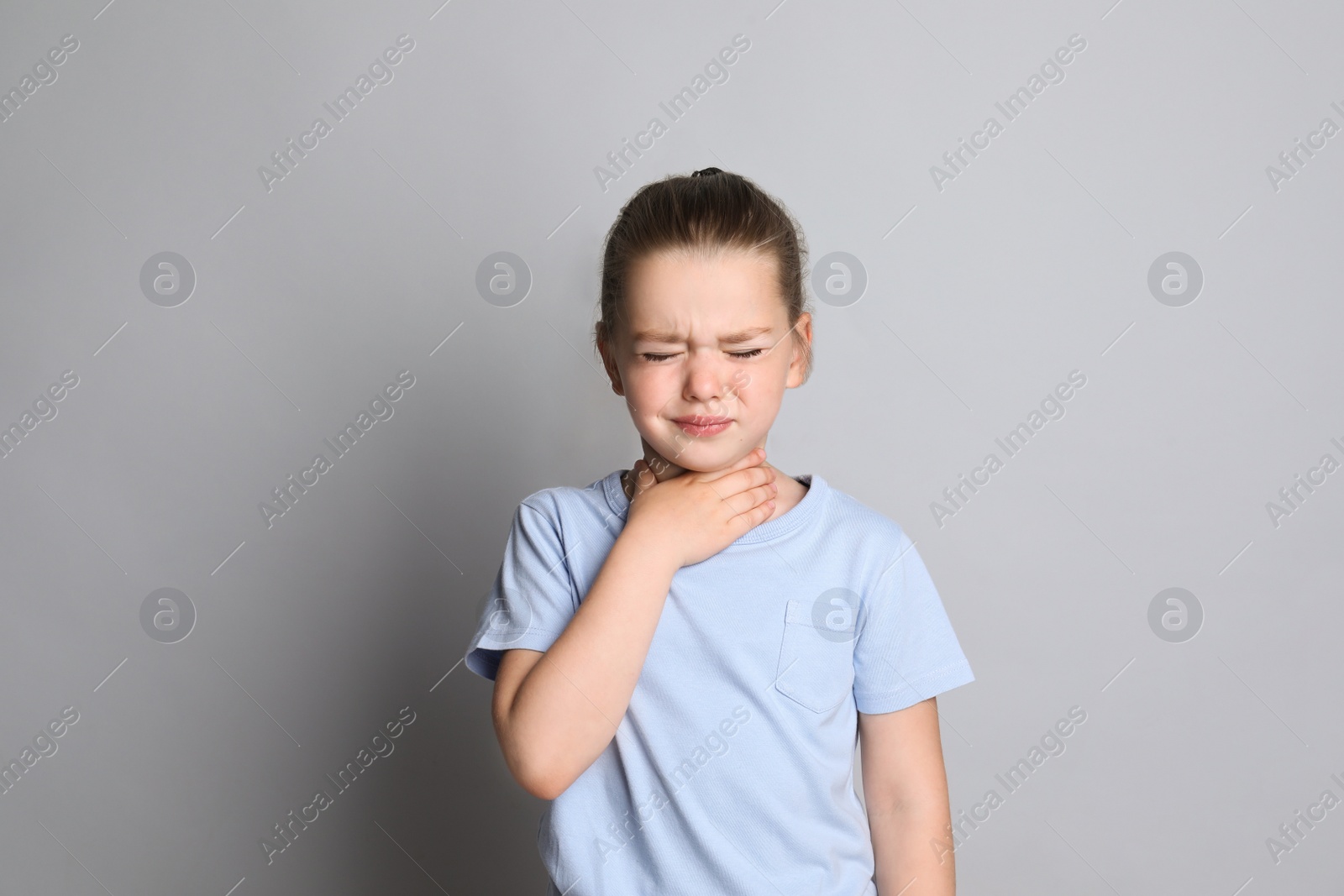 Photo of Little girl suffering from sore throat on grey background